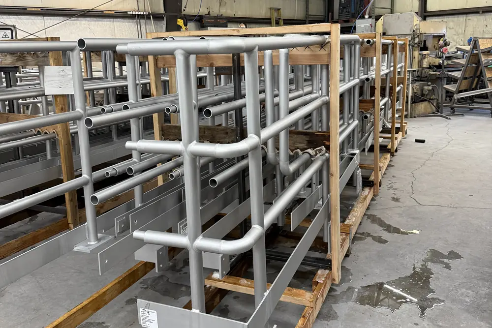 Rows of finished aluminum guardrail assemblies crated in timber frames down the length of the Logan shop floor