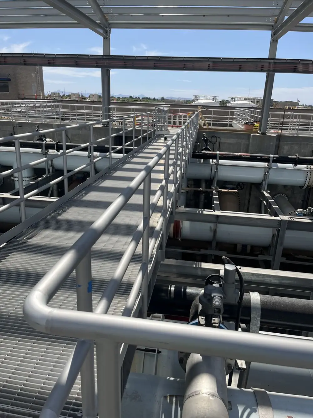 Aluminum guardrail and grating walkway running above process piping in late daylight
