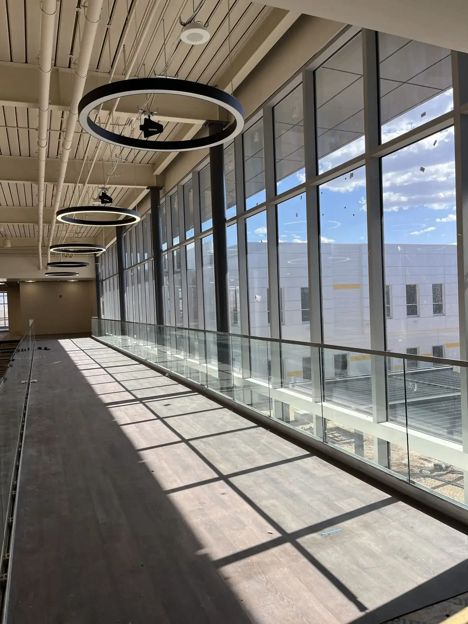 A long run of glass guardrail with stainless cap along a daylit upper corridor at Career Tech High School