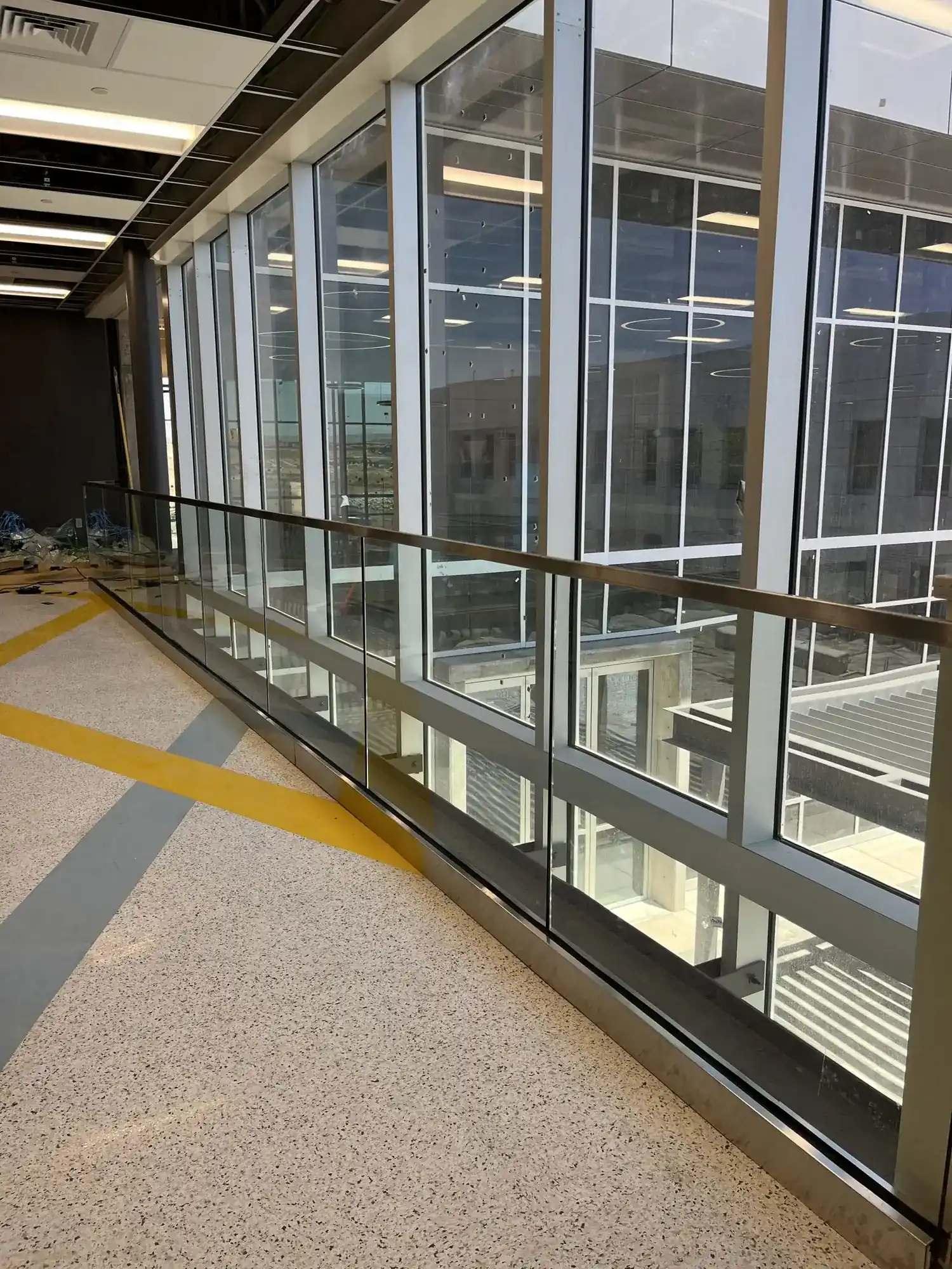 A long run of glass guardrail with stainless cap running the length of an upper corridor beside a full-height window wall