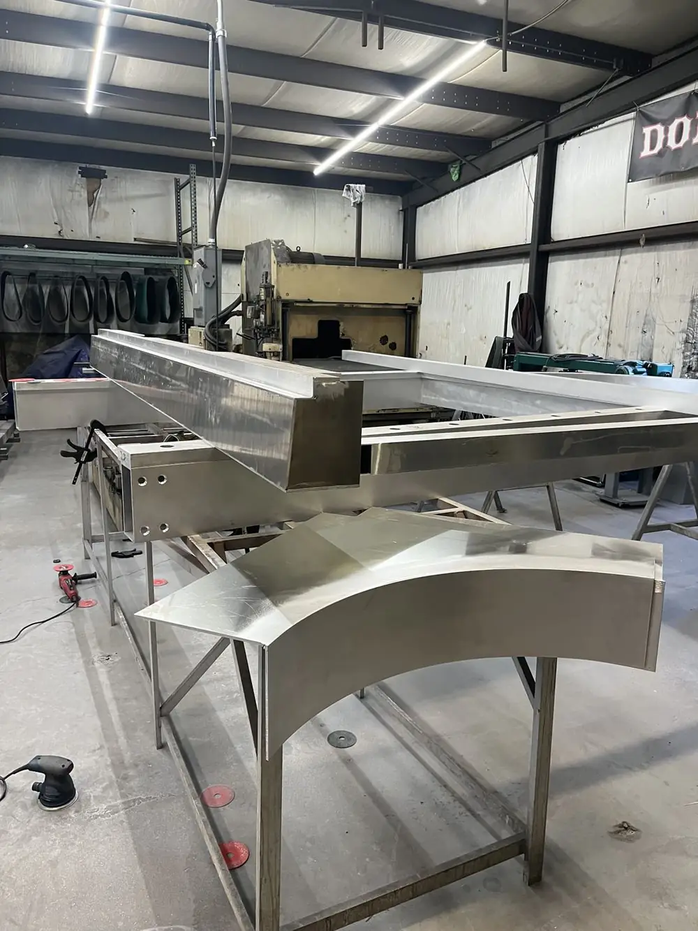 Long aluminum frame members and a curved arch section laid out on stands in the fabrication shop