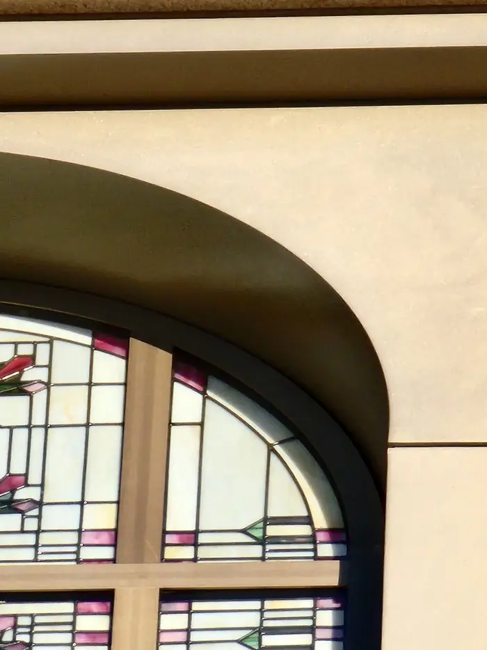 The head of an arched stained glass window meeting the cast stone opening