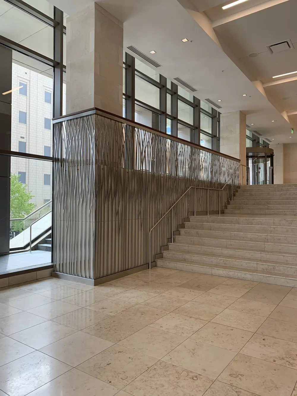 Twelve-foot brushed stainless grass-motif guardrail panel running alongside the finished lobby stair in KeyBank Tower at City Creek