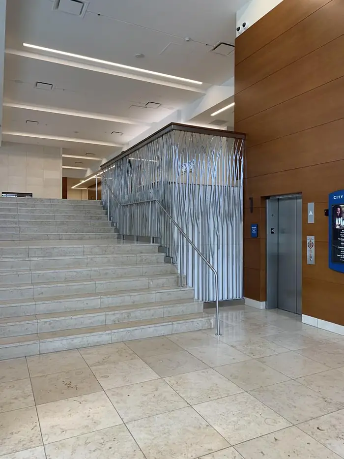 View up the KeyBank Tower lobby stair showing the grass-motif stainless panel above stone treads