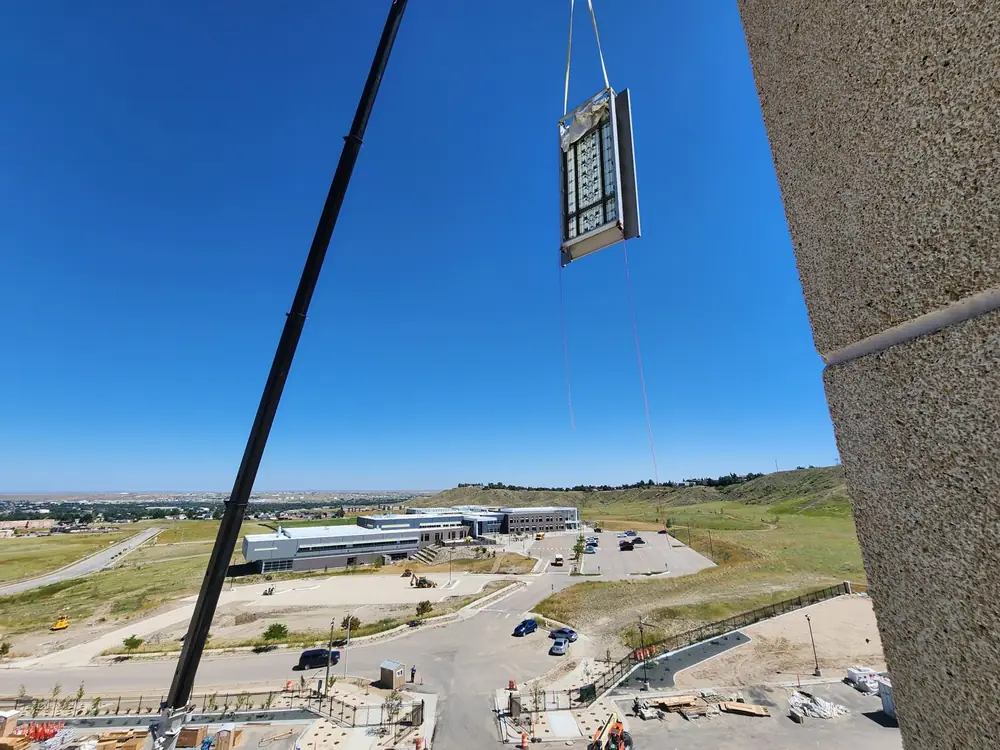A completed window frame assembly suspended on the crane line above the jobsite