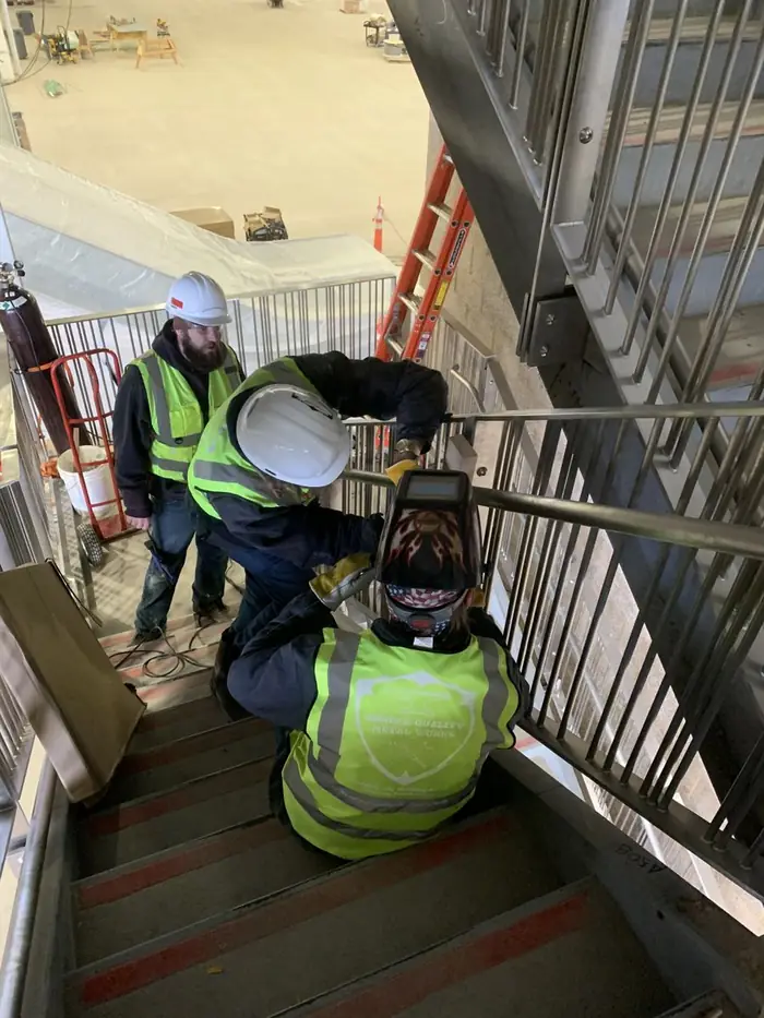 Two crew members welding stainless handrail on a stair in a parking structure