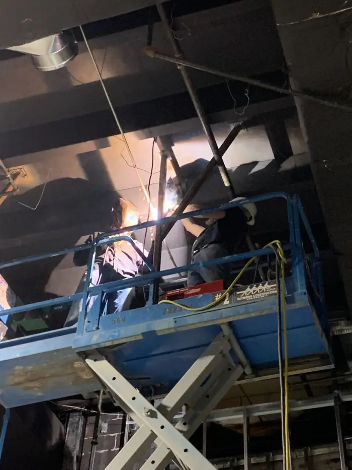 A welder working overhead from a scissor lift, sparks falling