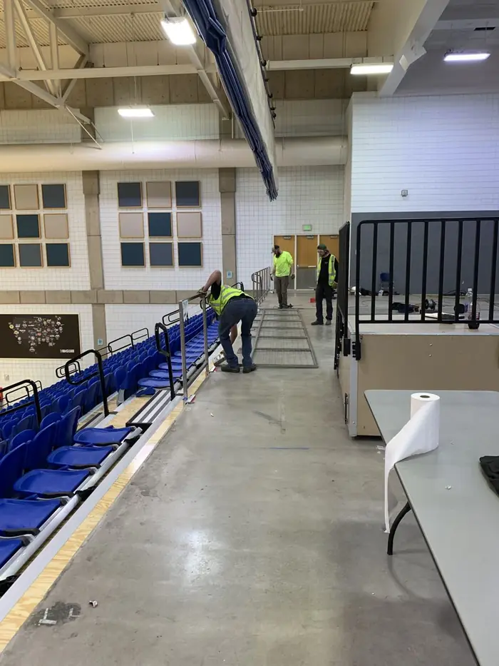 Crew installing guardrail along a bleacher edge in a field house