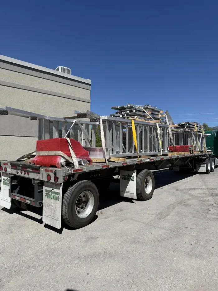 Flatbed trailer loaded and strapped with anodized aluminum rail and stair assemblies outside the Logan shop