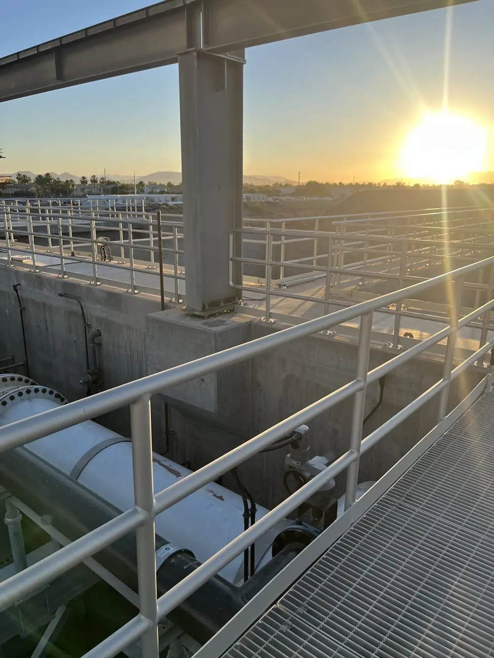 Sun setting through the plant structure over guardrail, grating and process piping