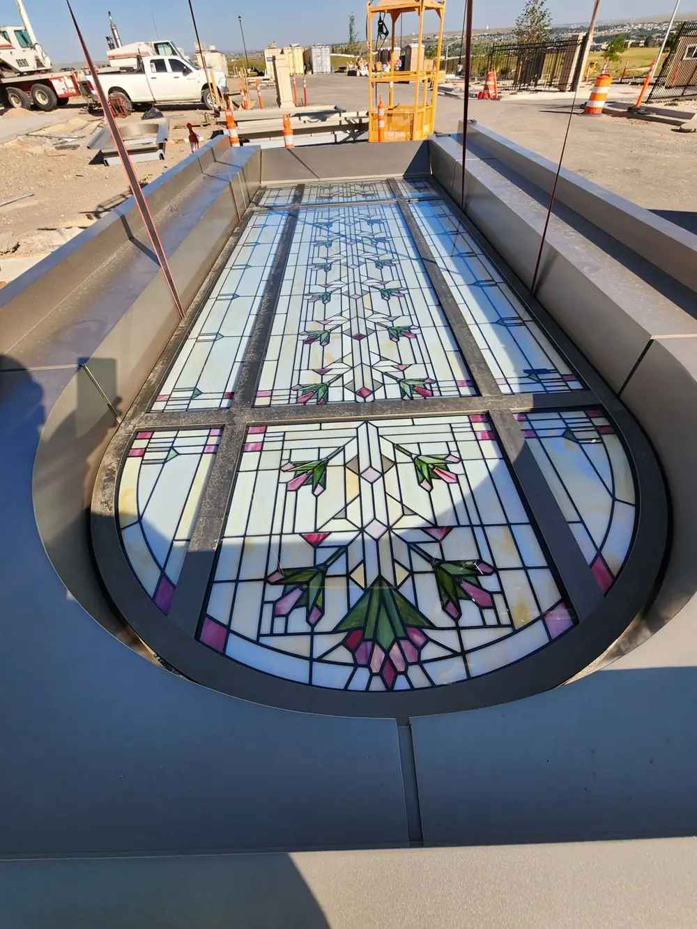 An arched stained glass panel glazed into its aluminum frame, laid flat before the lift
