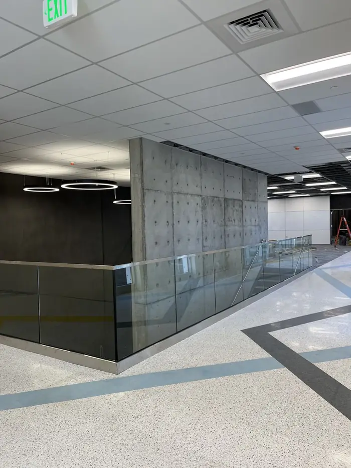 Glass guardrail wrapping a mezzanine edge past a board-formed concrete wall