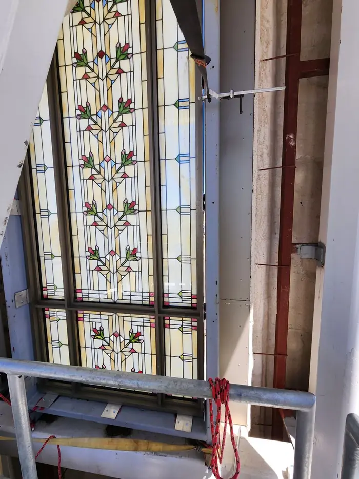 A tall stained glass window set in its finished aluminum frame