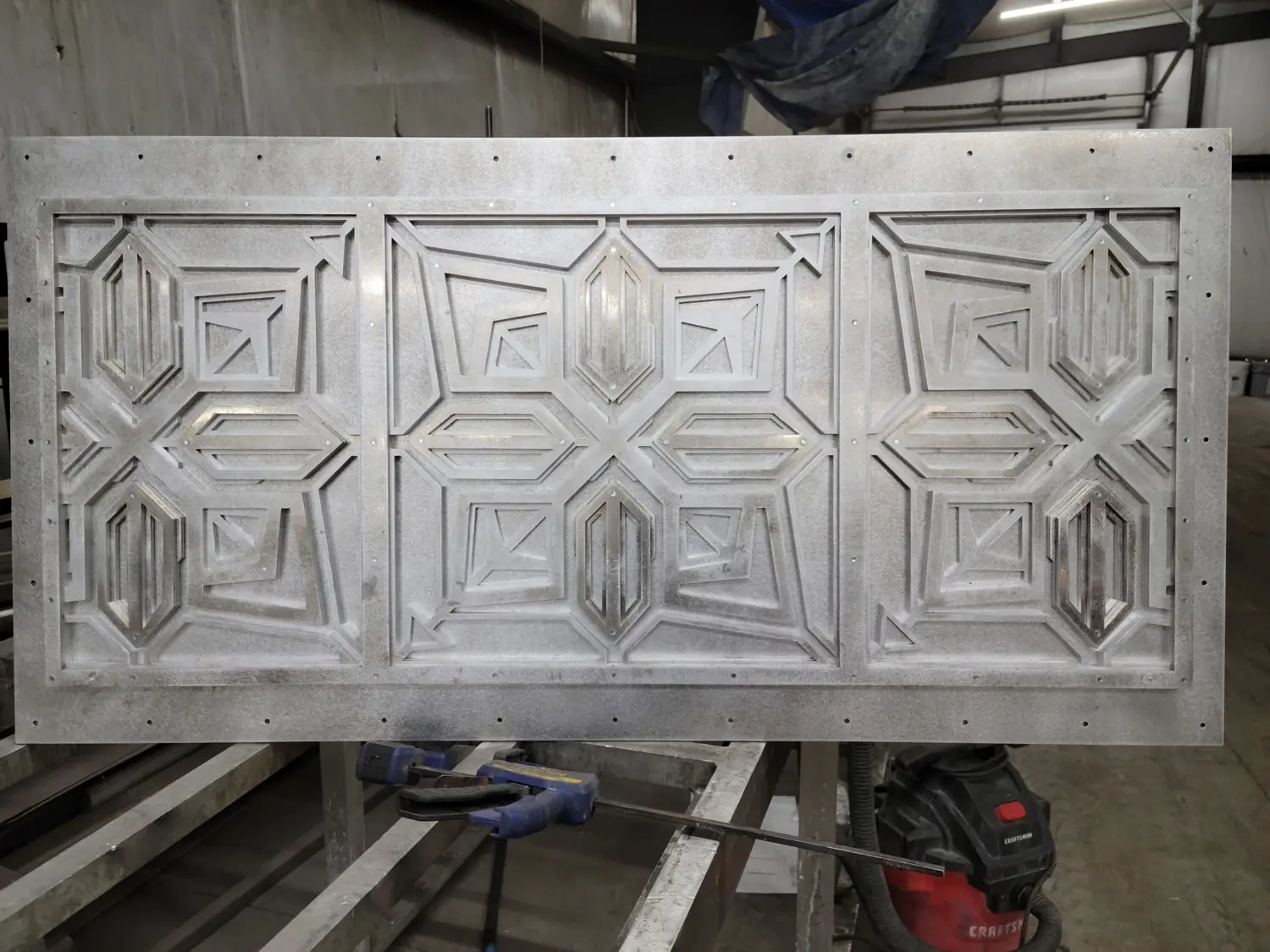 A decorative window transom panel in bare aluminum, built from layers of laser-cut plate in a geometric pattern