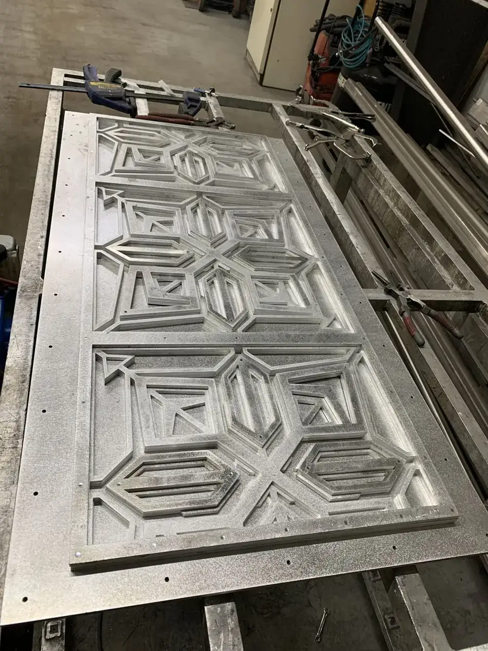 A full transom panel laid out in the shop before finishing, the layered geometric relief visible in raw aluminum