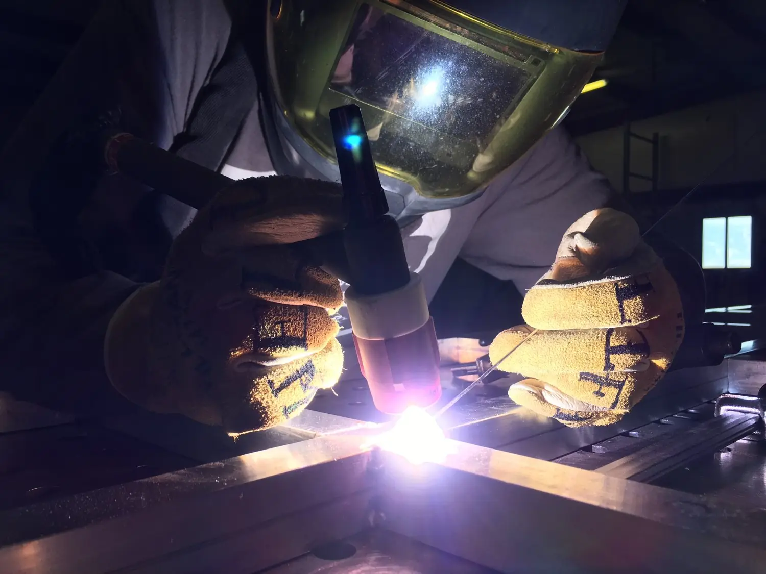 A welder laying a TIG bead, hood down, the arc burning bright against the metal