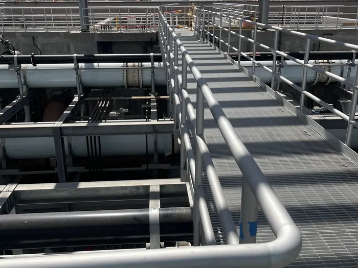 Aluminum guardrail along an elevated grating walkway above a pressurized pipe gallery
