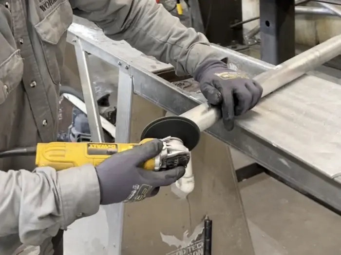 Gloved hands running an abrasive disc along an aluminum rail section in the shop
