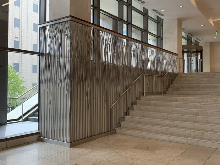 Brushed stainless grass-motif guardrail panels running the length of a travertine lobby stair