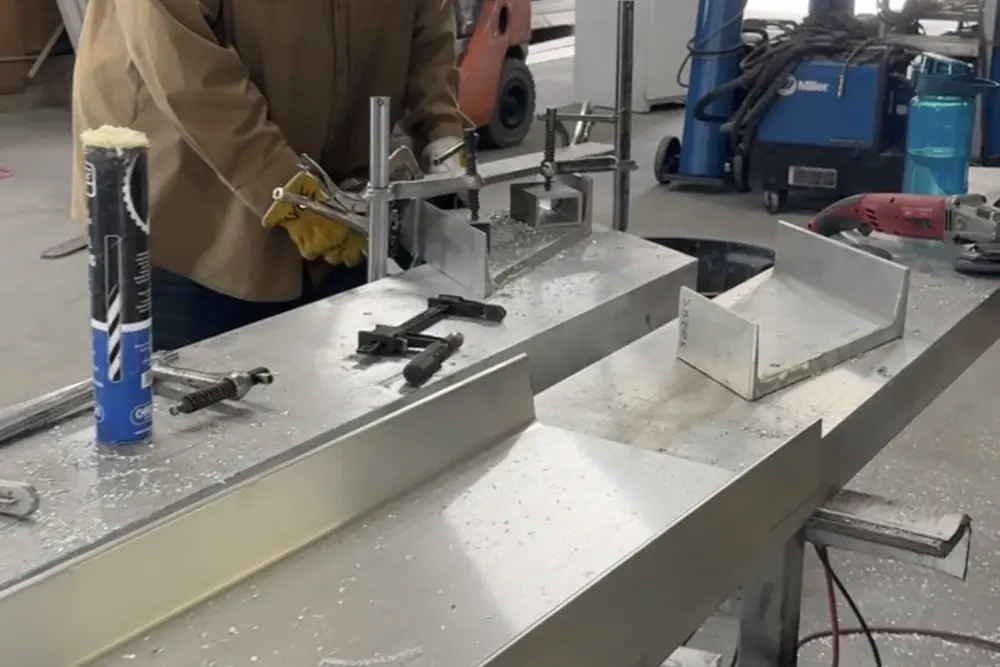 A long aluminum section clamped on the bench mid-fabrication, swarf and layout tools around it