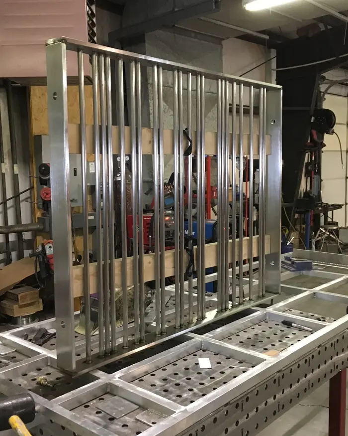 A stainless guardrail panel clamped upright on the fixture table in the Logan shop