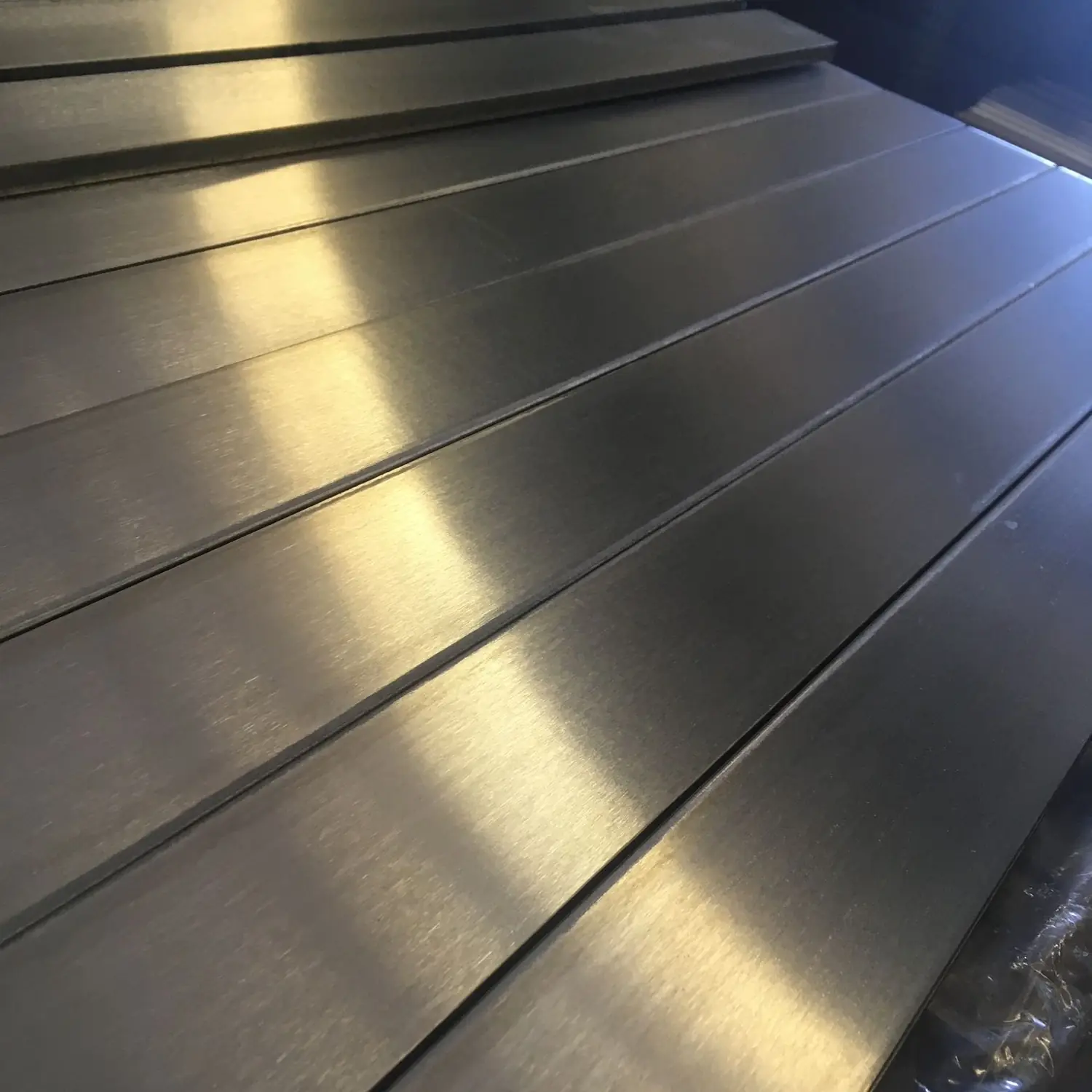 Brushed stainless plate stacked in raking light, the grain running the length of each piece
