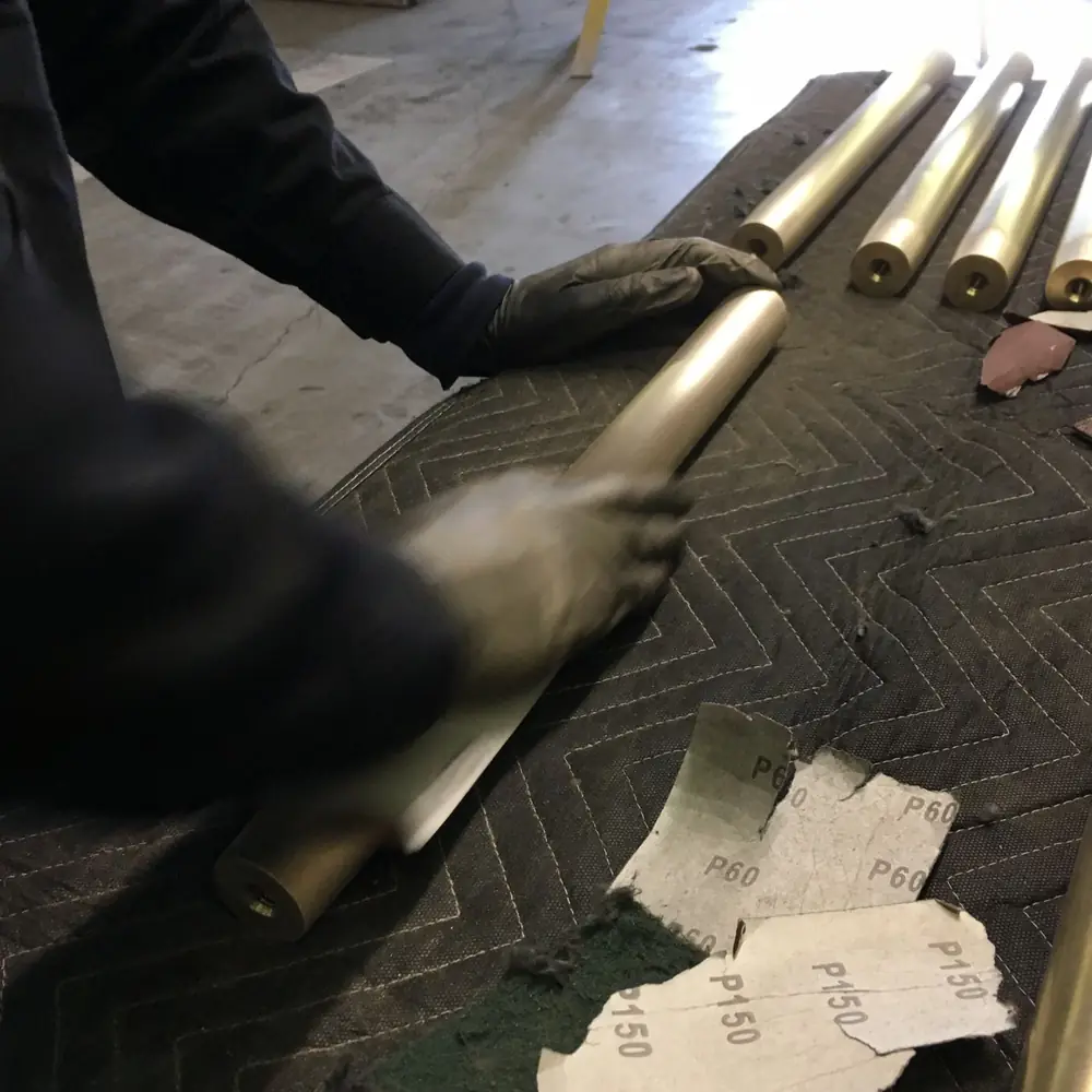 Gloved hands working abrasive paper along a bronze rail section, grit sheets laid out alongside