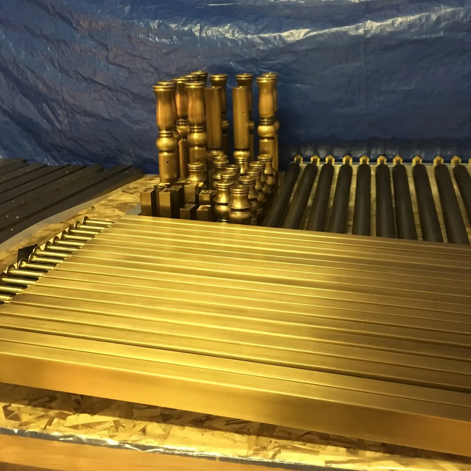 Rows of architectural bronze rail stock and newel components in the shop under warm light