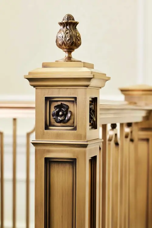 Finished bronze newel post with cast finial and ornamental panel detail installed at the temple
