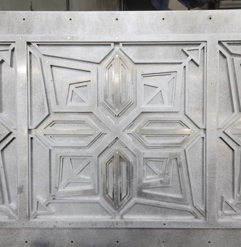 A decorative transom panel built from layers of laser-cut aluminum plate in a geometric relief pattern