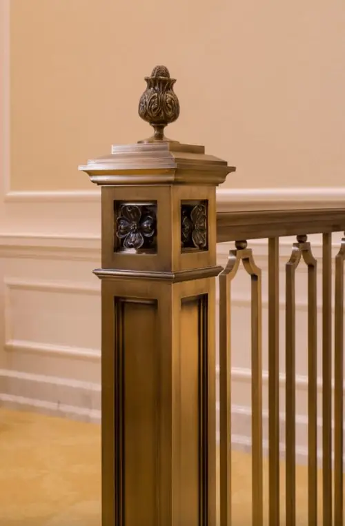 A finished architectural bronze newel post with cut flower panels set into the post and an ornamental finial above