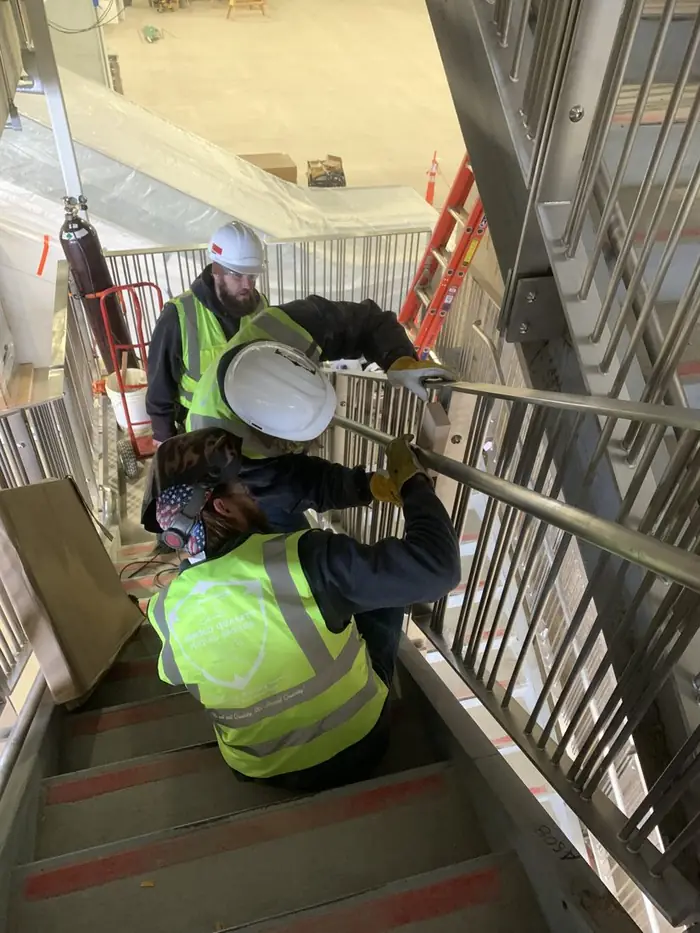 Two Arnold Quality crew members in hi-vis and hard hats working on a stair handrail installation