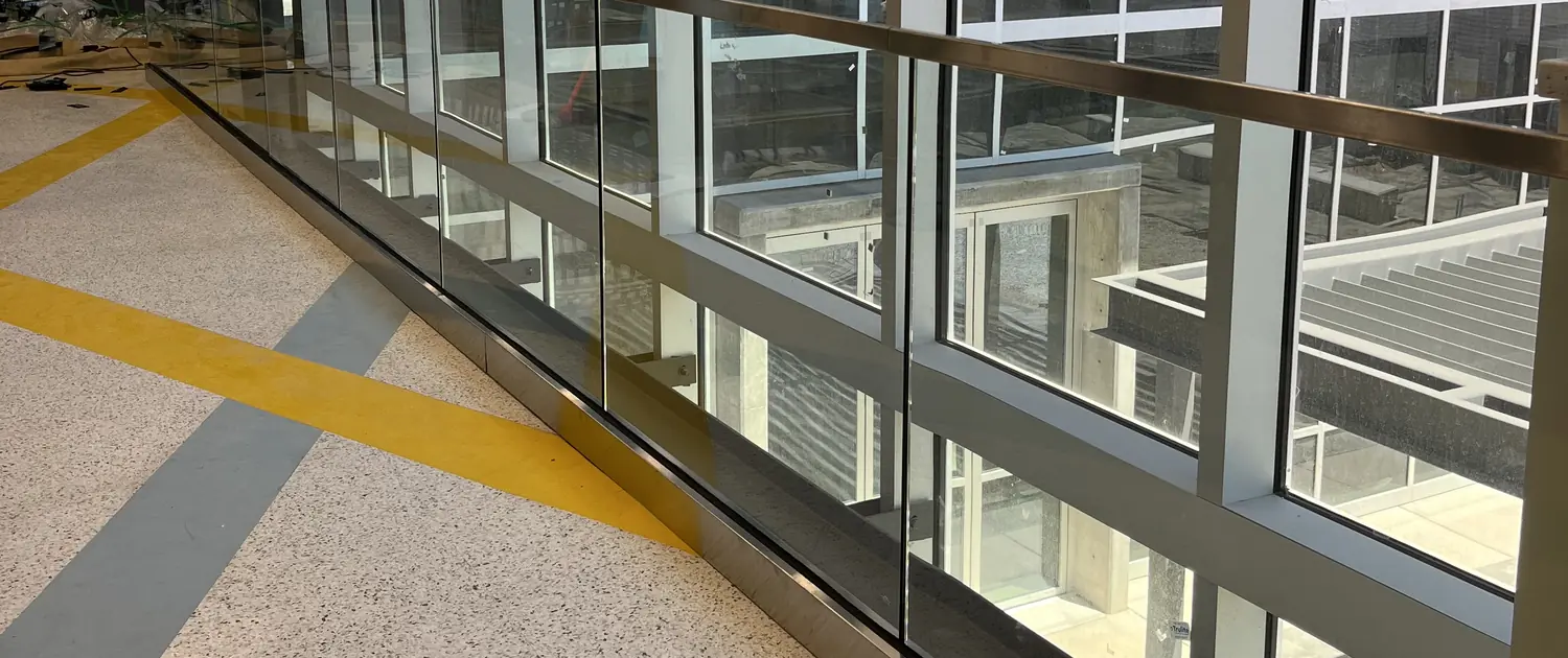A long run of glass guardrail with a brushed stainless cap rail receding along a finished mezzanine edge