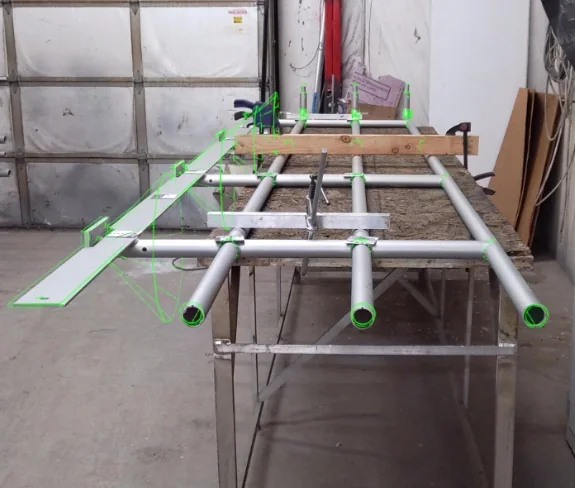 The FabStation augmented reality overlay projected onto an aluminium rail assembly on the fixture table, the green model wireframe sitting over the real tube and plate
