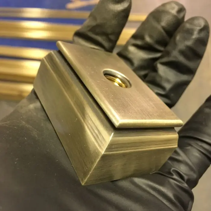 Gloved hand holding a patinated bronze base component with a machined opening