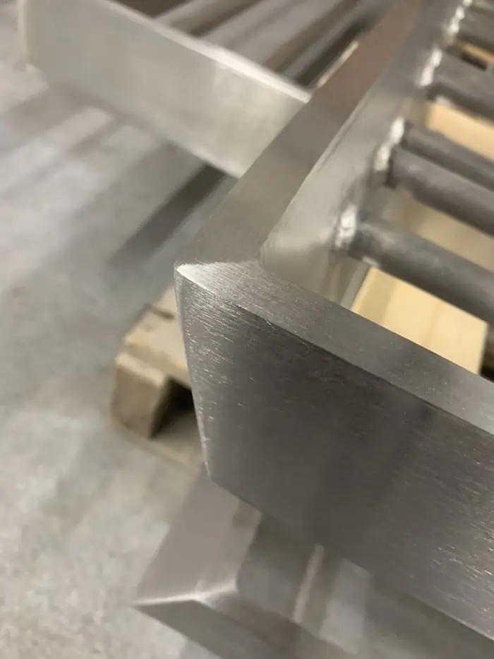 Mitered corner of a stainless flatbar rail frame, hand polished so the satin grain runs unbroken around the return and the corner weld is fully blended