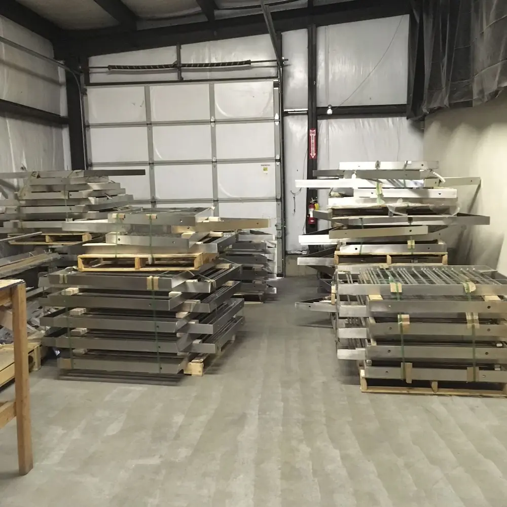 A shop bay filled with pallets of finished stainless rail panels, stacked and banded