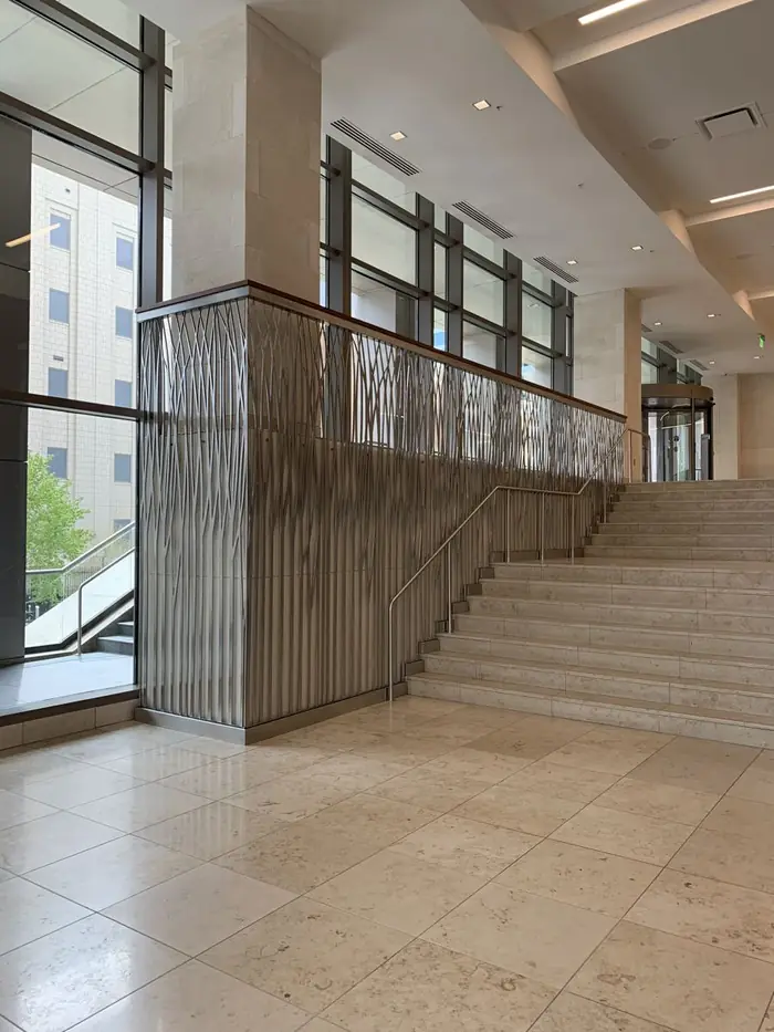 Stainless grass-motif infill panels along a stair in a tower lobby