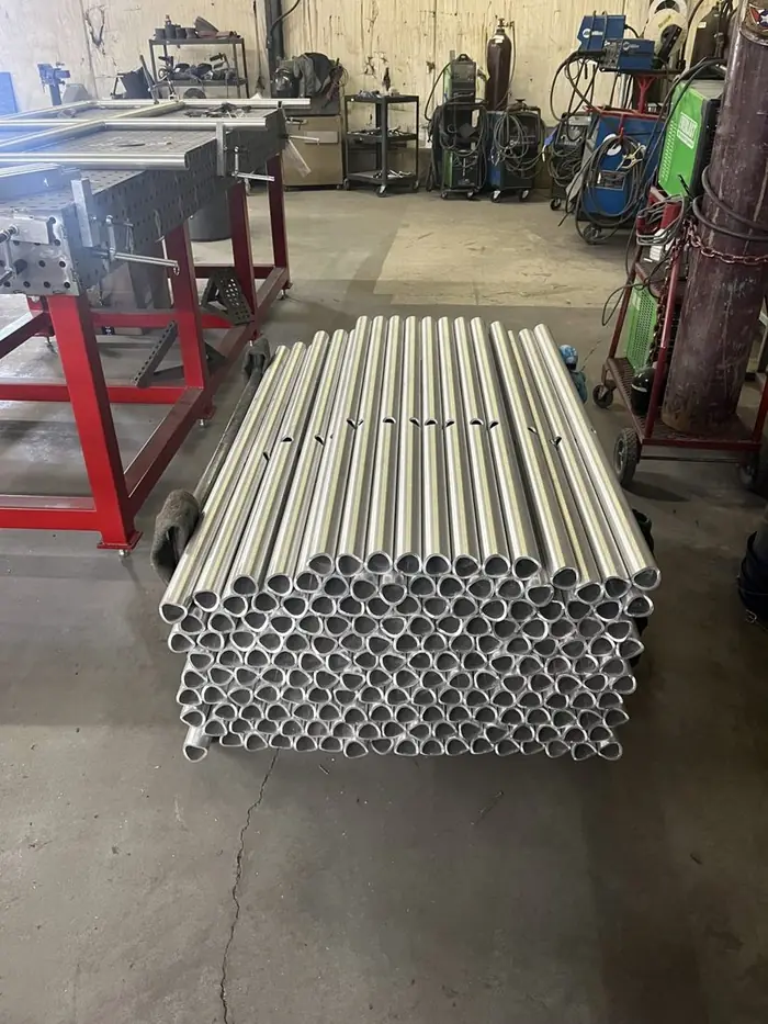 A stacked bundle of aluminum tube cut, coped and drilled for guardrail assembly on the shop floor